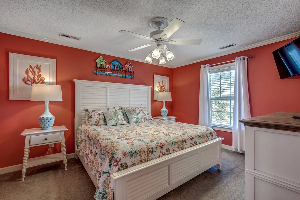 A cheerful bedroom adorned with floral bedding, colorful wall art, and blue-accented lamps on white furniture. The room is filled with soft, natural light, offering a restful retreat after a day of adventure.