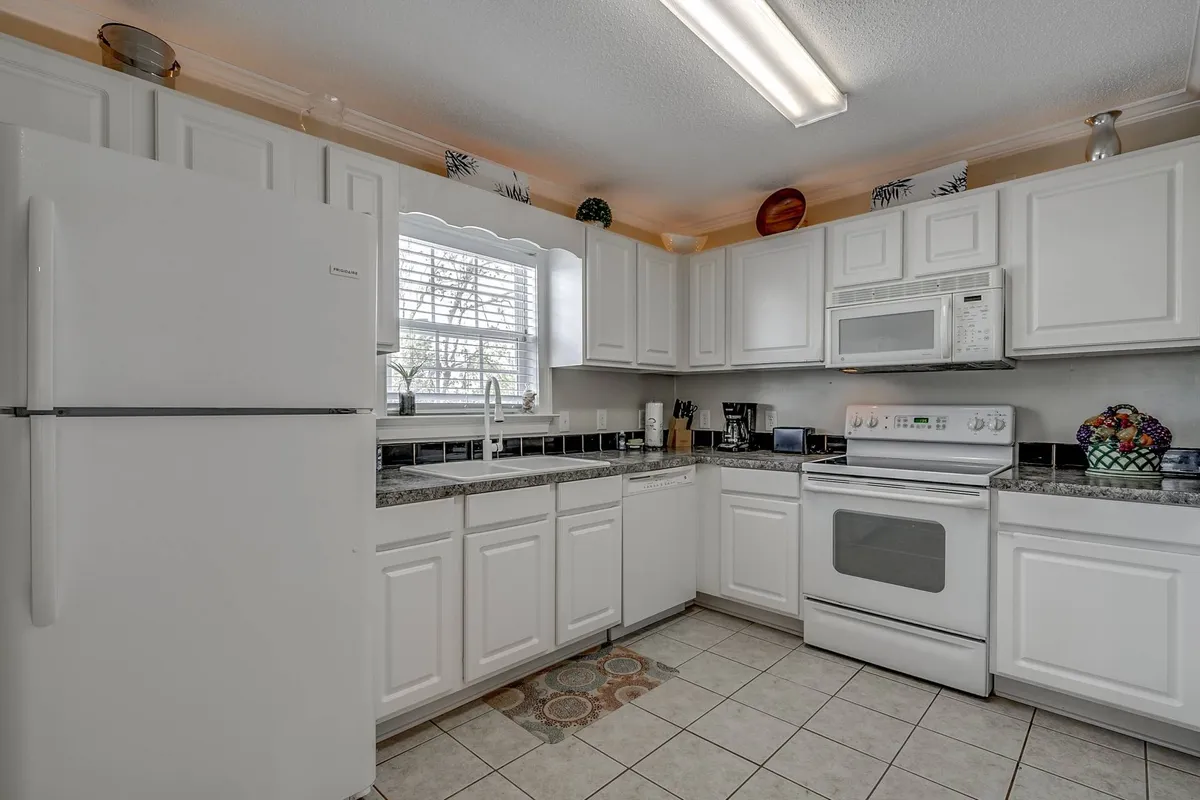 This image features a welcoming kitchen with white cabinets, granite countertops, modern appliances, and a window that fills the space with natural light. The scene captures an inviting spot where family and friends can gather to cook, bake, and socialize.