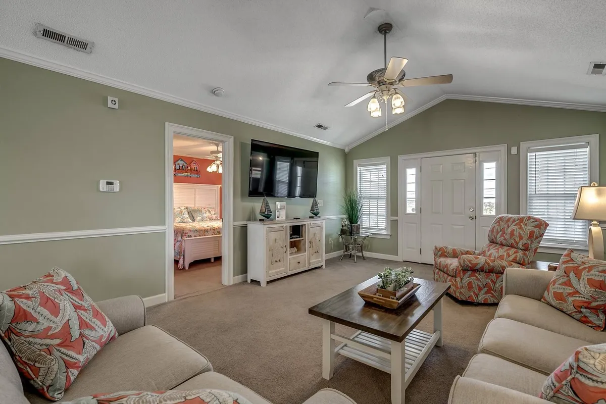 A spacious, sunlit living room featuring a comfortable sofa, decorative armchairs, a TV unit, and a coffee table with tasteful decor. The room is arranged to accommodate family gatherings, game nights, or relaxing evenings watching movies together.
