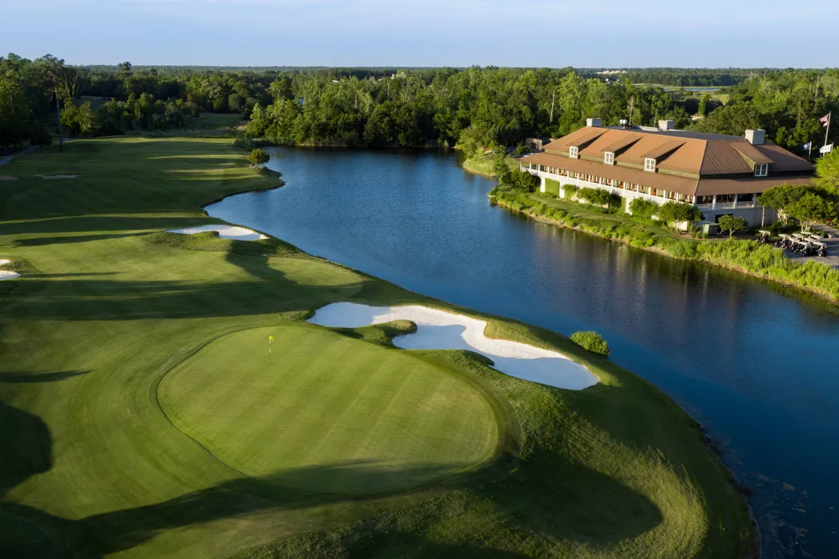 A sweeping exterior view of a lush golf course, complete with rolling greens, a tranquil lake, and a welcoming clubhouse. The landscape is bathed in soft sunlight, suggesting a peaceful morning or evening perfect for a round of golf or relaxing by the water.