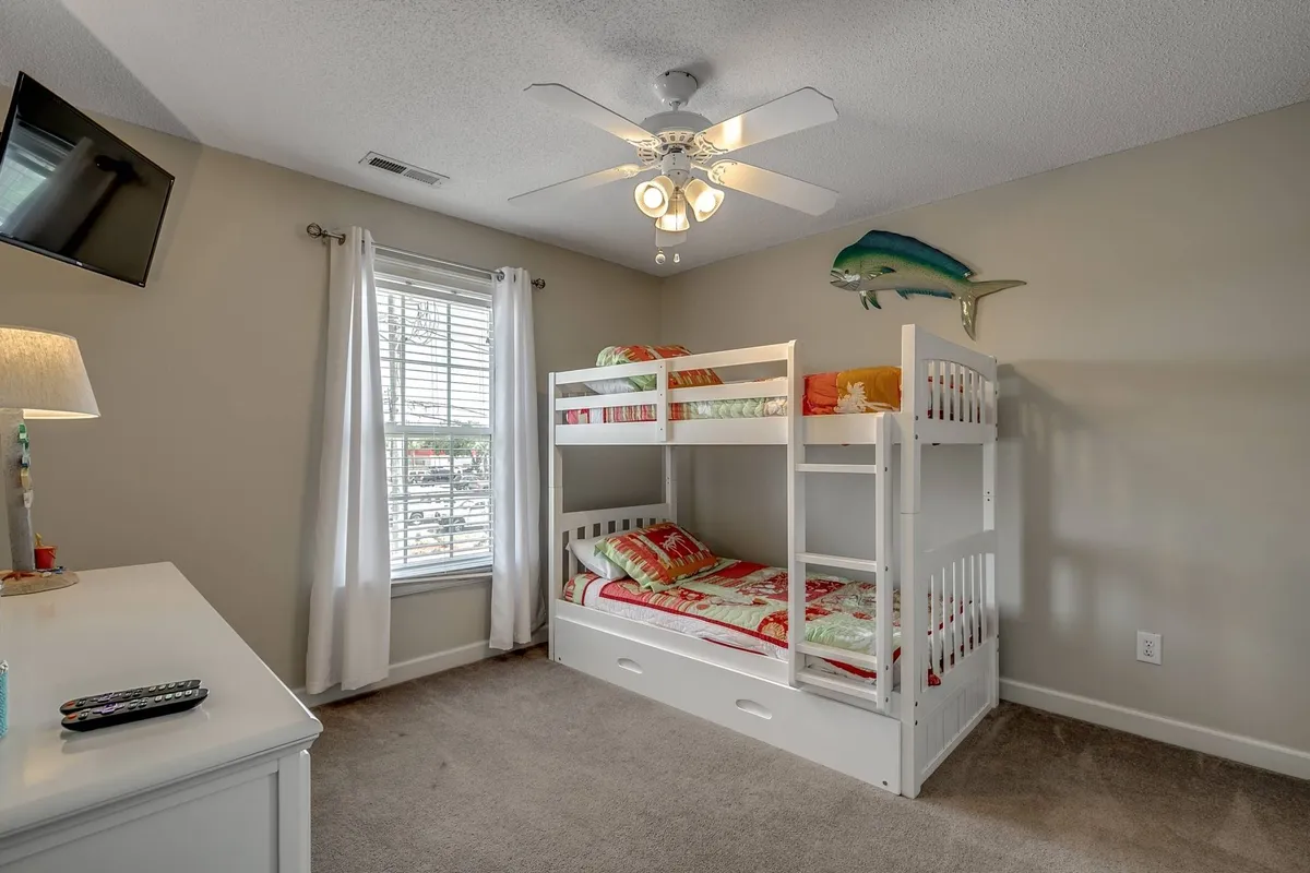 A playful kids’ bedroom with a bunk bed, window with curtains, ceiling fan, and decorative fish accents. The light-filled space is perfect for sleepovers, imaginative play, or quiet reading moments.